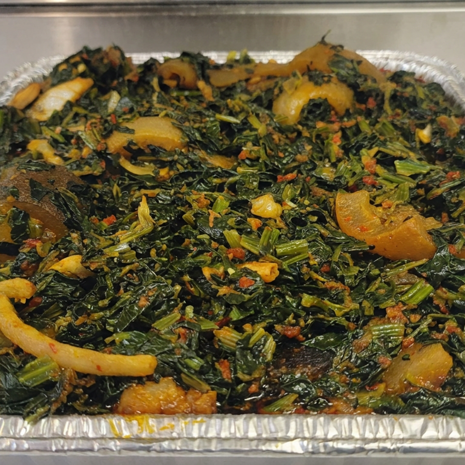 Aluminum catering tray filled with seasoned leafy greens, sliced vegetables, and orange chunks.